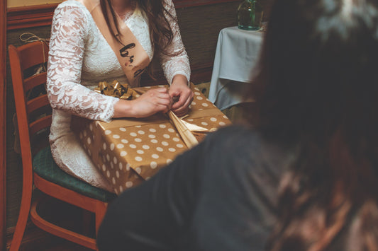woman wearing white dress setting on a chair opening a golden gift