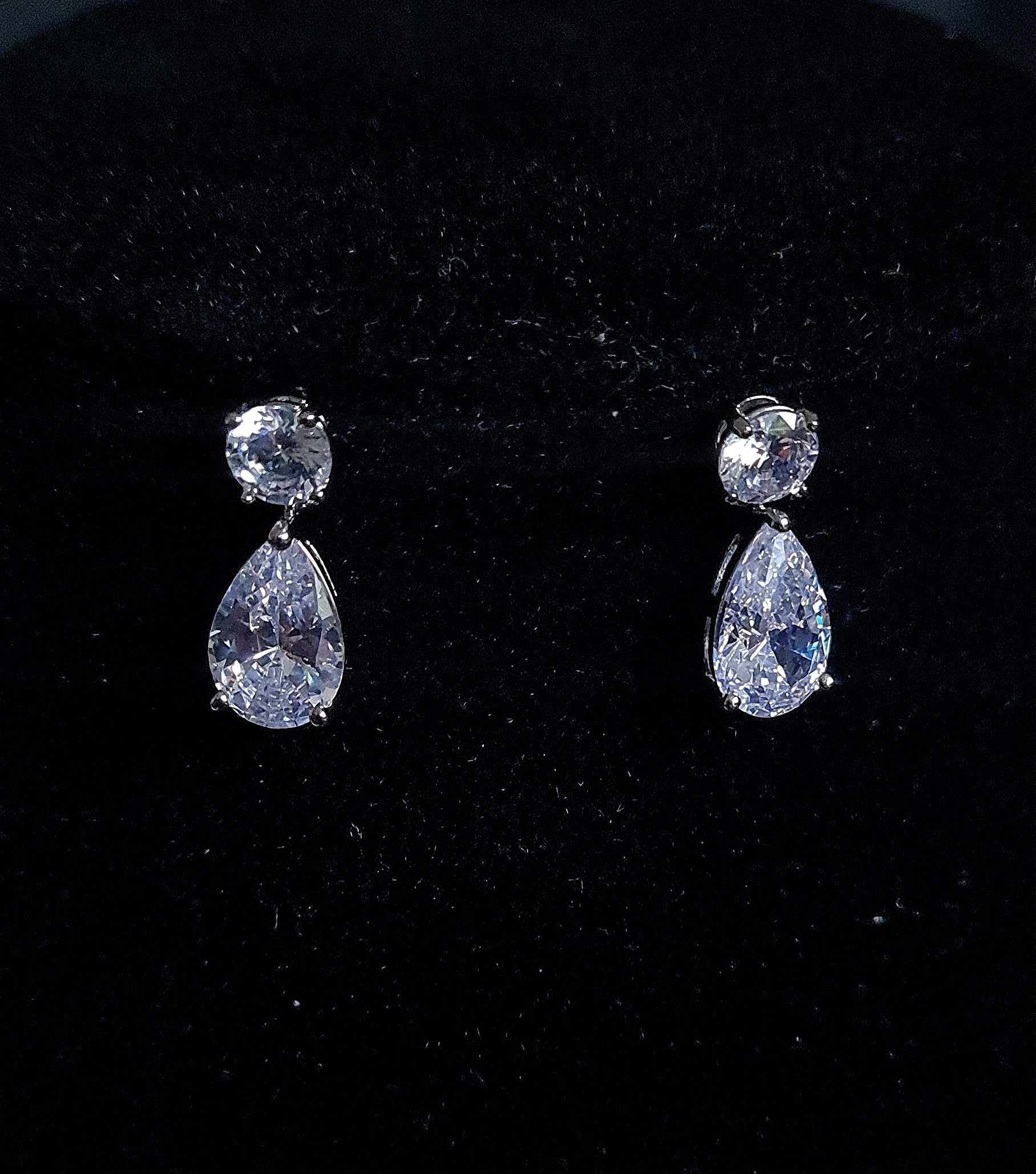 A pair of mini earrings studded with cubic zirconia crystals Placed on black table.