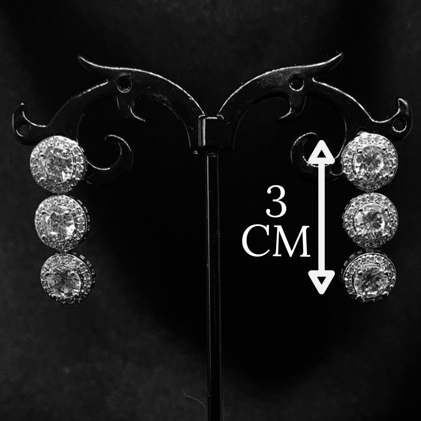 A pair of dangle earrings made of cubic zirconia. The earrings are round-shaped and have a simple, elegant design. The cubic zirconia stones are clear and sparkling. The earrings are hanging from a black metal wire. with measure.