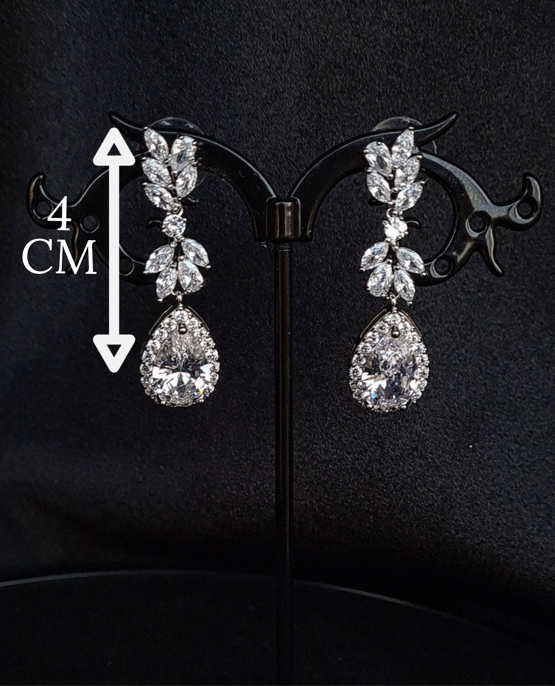 A pair of silver earrings with dangling teardrop pearls. The earrings are simple in design and the pearls are lustrous. The earrings are a perfect accessory for a special occasion or a gift for a loved one. with measures.