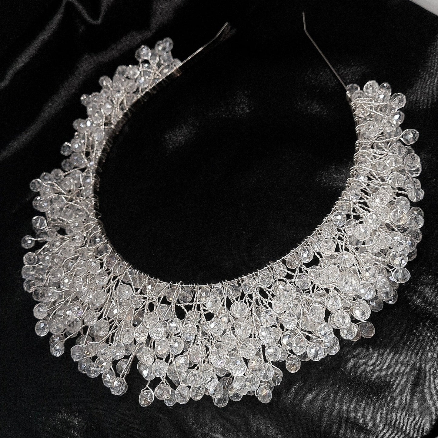 a bridal hair piece on a black background. The hair piece is made of pearls and crystals, and it has a delicate, feminine design. It is perfect for a bride who wants to add a touch of elegance to her wedding day look. The hair piece is shown on a black background, so the pearls and crystals stand out beautifully