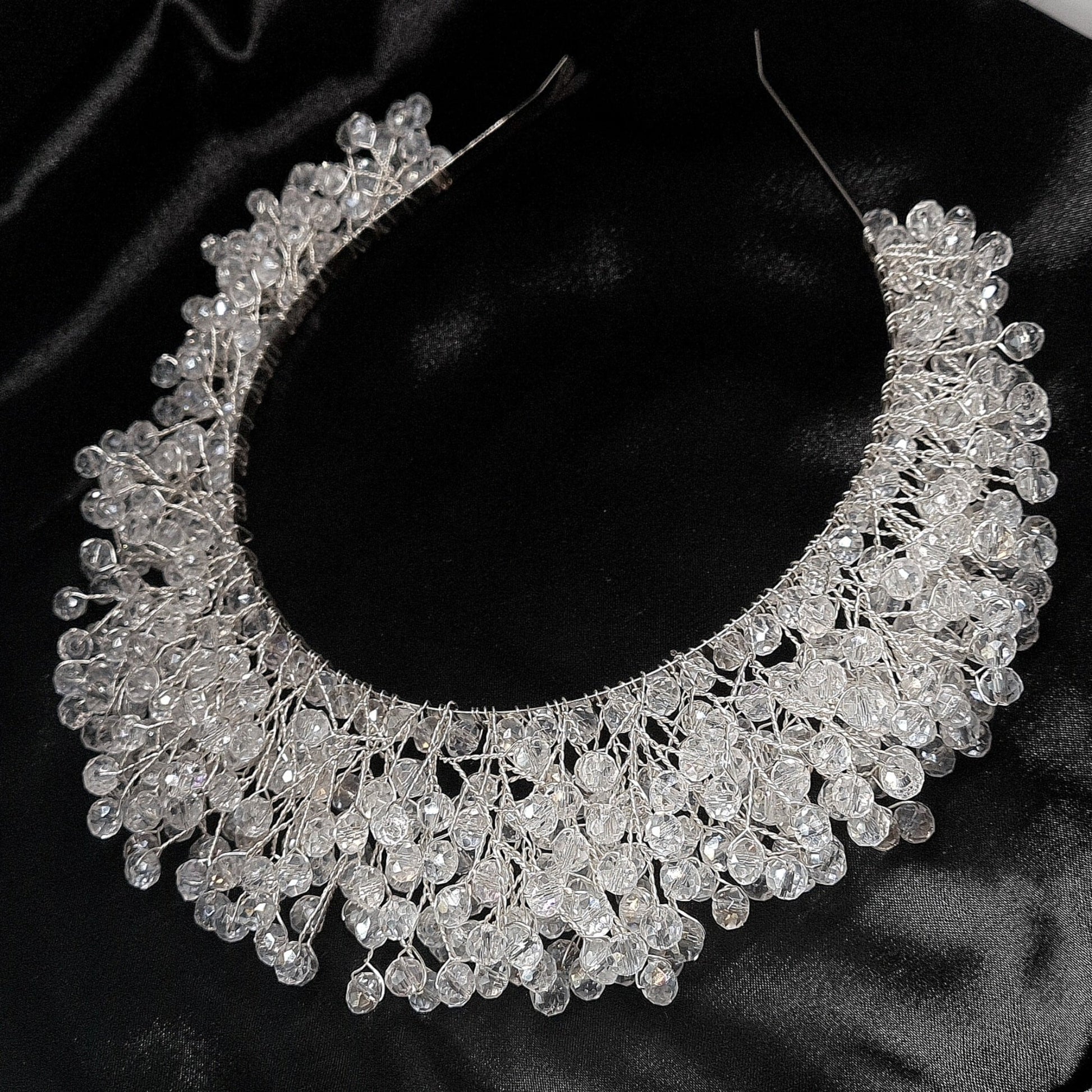 a bridal hair piece on a black background. The hair piece is made of pearls and crystals, and it has a delicate, feminine design. It is perfect for a bride who wants to add a touch of elegance to her wedding day look. The hair piece is shown on a black background, so the pearls and crystals stand out beautifully