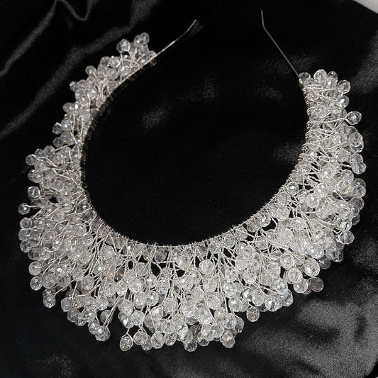 a bridal hair piece on a black background. The hair piece is made of pearls and crystals, and it has a delicate, feminine design. It is perfect for a bride who wants to add a touch of elegance to her wedding day look. The hair piece is shown on a black background, so the pearls and crystals stand out beautifully