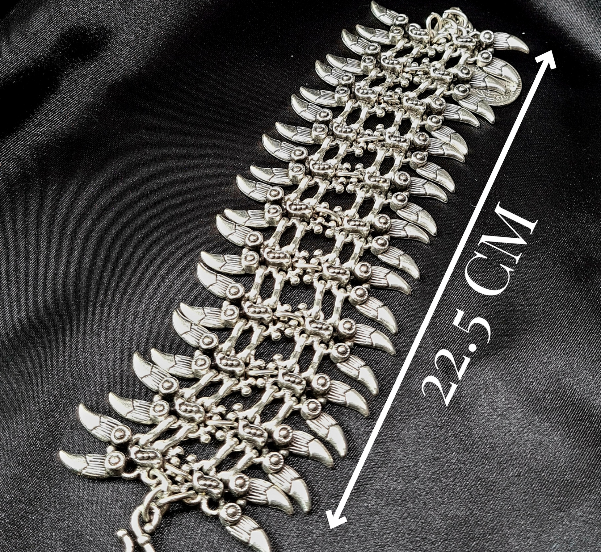 A silver bracelet with a claw design on it. The bracelet is made of silver and has a delicate design. The claw design is in the center of the bracelet and is made up of small, interlocking pieces. The bracelet is sitting on a black cloth with length.
