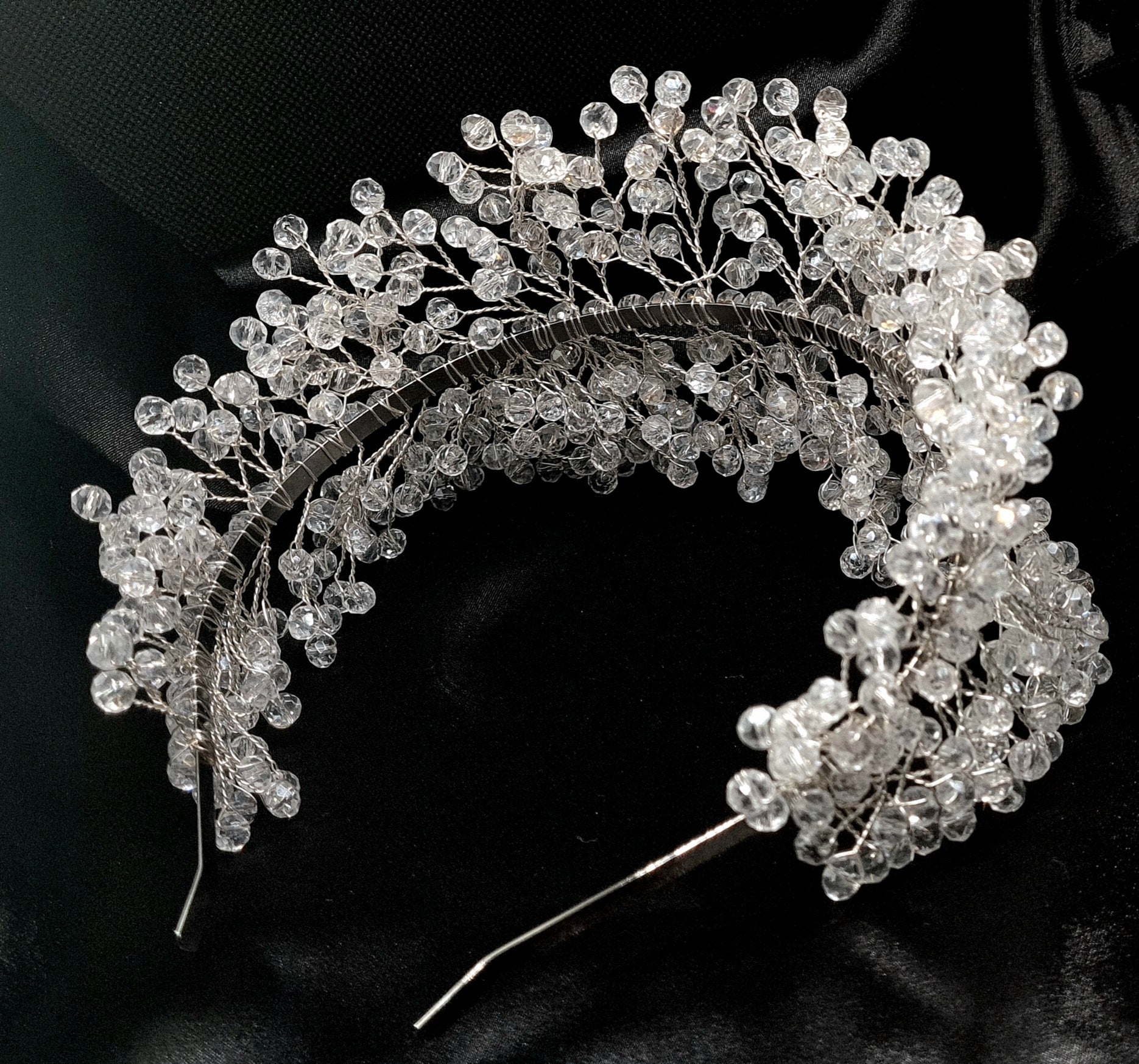 a bridal hair piece on a black background. The hair piece is made of pearls and crystals, and it has a delicate, feminine design. It is perfect for a bride who wants to add a touch of elegance to her wedding day look. The hair piece is shown on a black background, so the pearls and crystals stand out beautifully