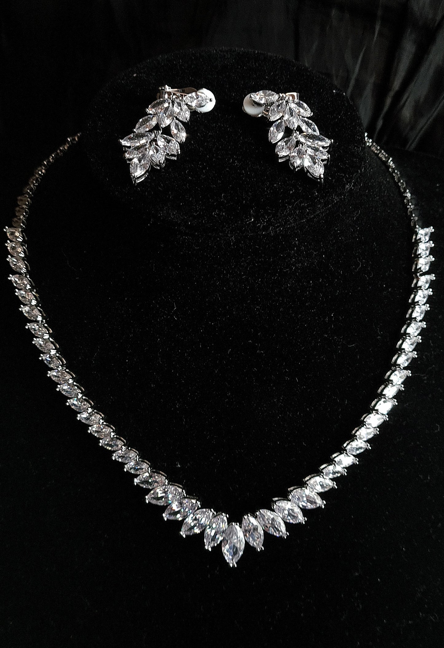 Black Mannequin Displaying a Stylish Cubic Zirconia Necklace and Earring Jewelry Set with Marquise Cut Design. The Necklace Showcases a Brilliant Marquise Shape Cut CZ Pendant, Complemented by Dangle Drop Earrings of Matching Design. All Set Against a Sleek Black Background,
