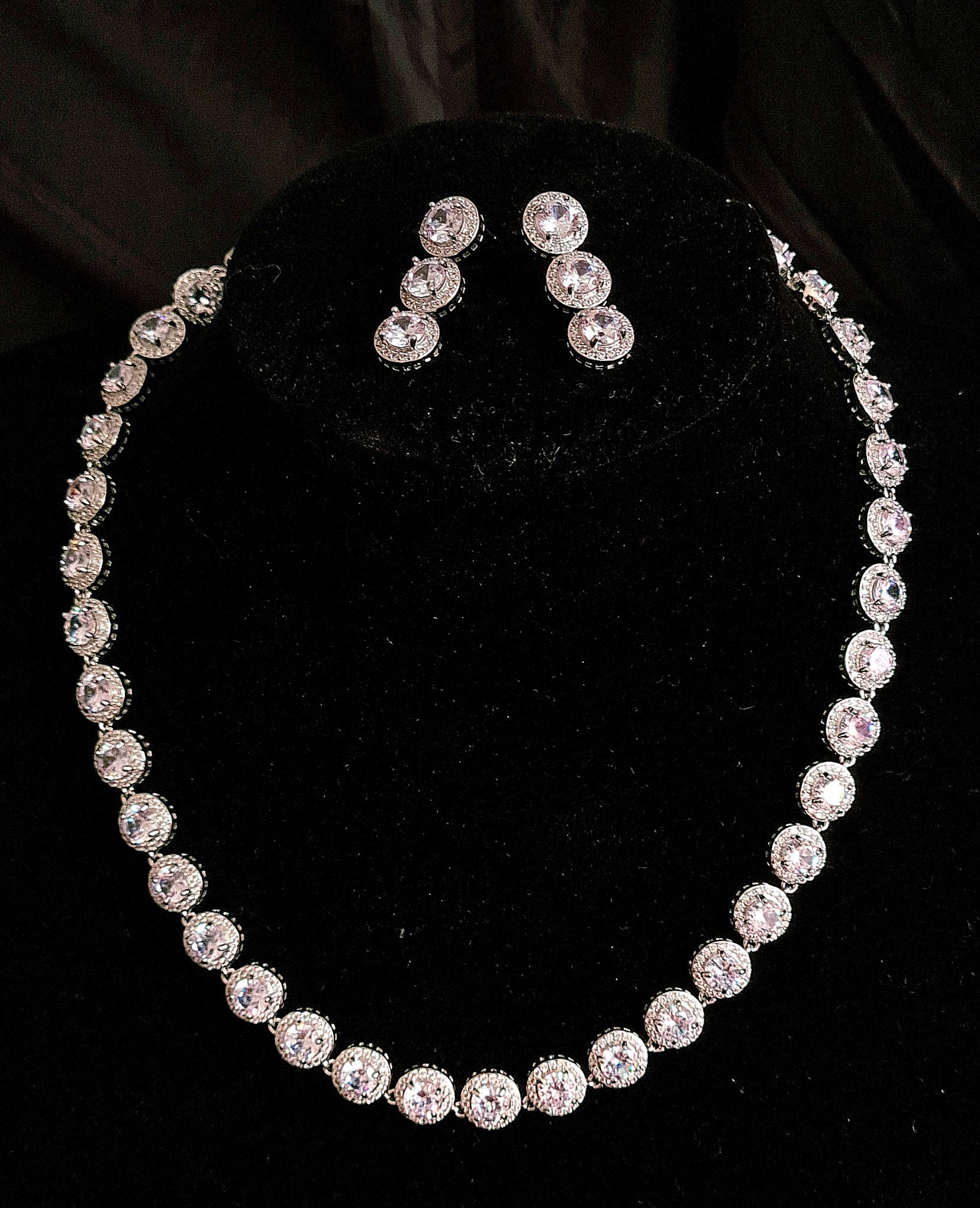 Graceful Black Mannequin Displaying a Stylish Cubic Zirconia Necklace and Earring Jewelry Set with Round Cut Stones. The Necklace Features Shimmering Round Cut CZ Pendant, Complemented by Dangle Drop Earrings Adorned with Matching Round Cut CZs. Against a Sleek Black Background.