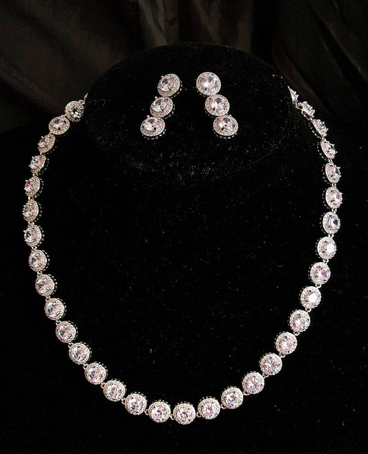 Graceful Black Mannequin Displaying a Stylish Cubic Zirconia Necklace and Earring Jewelry Set with Round Cut Stones. The Necklace Features Shimmering Round Cut CZ Pendant, Complemented by Dangle Drop Earrings Adorned with Matching Round Cut CZs. Against a Sleek Black Background.