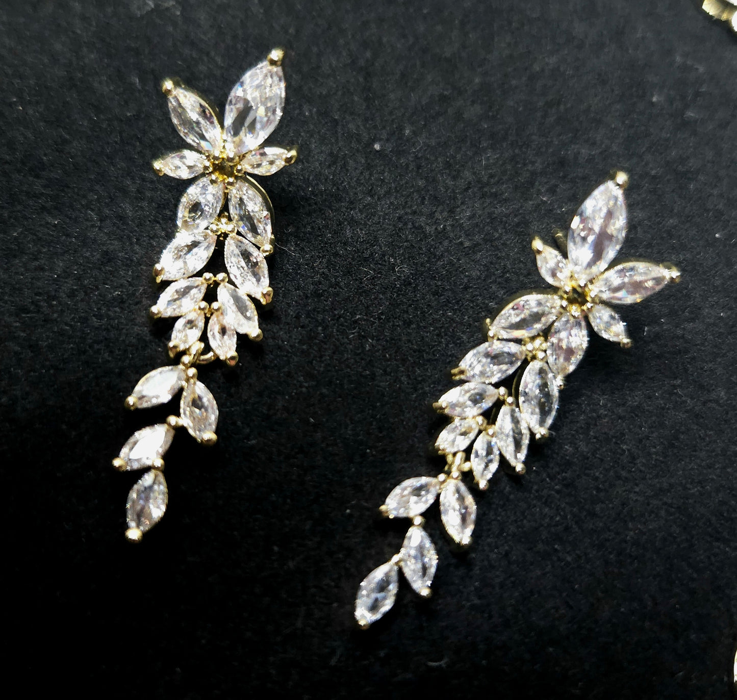 An elegant, high-definition close-up of the La Pasión Regal Gold earrings. The botanical marquise-cut stones are displayed to showcase their diamond-simulated brilliance and fine gold-tone setting, embodying a sophisticated, high-fashion jewelry aesthetic.