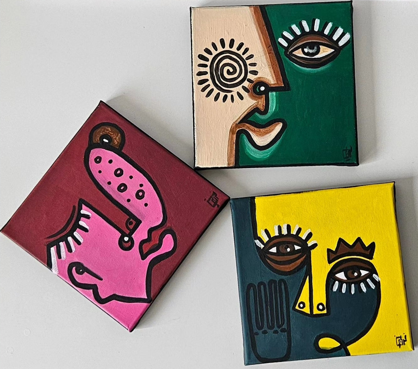 Three abstract paintings with stylized faces in different colors and shapes.