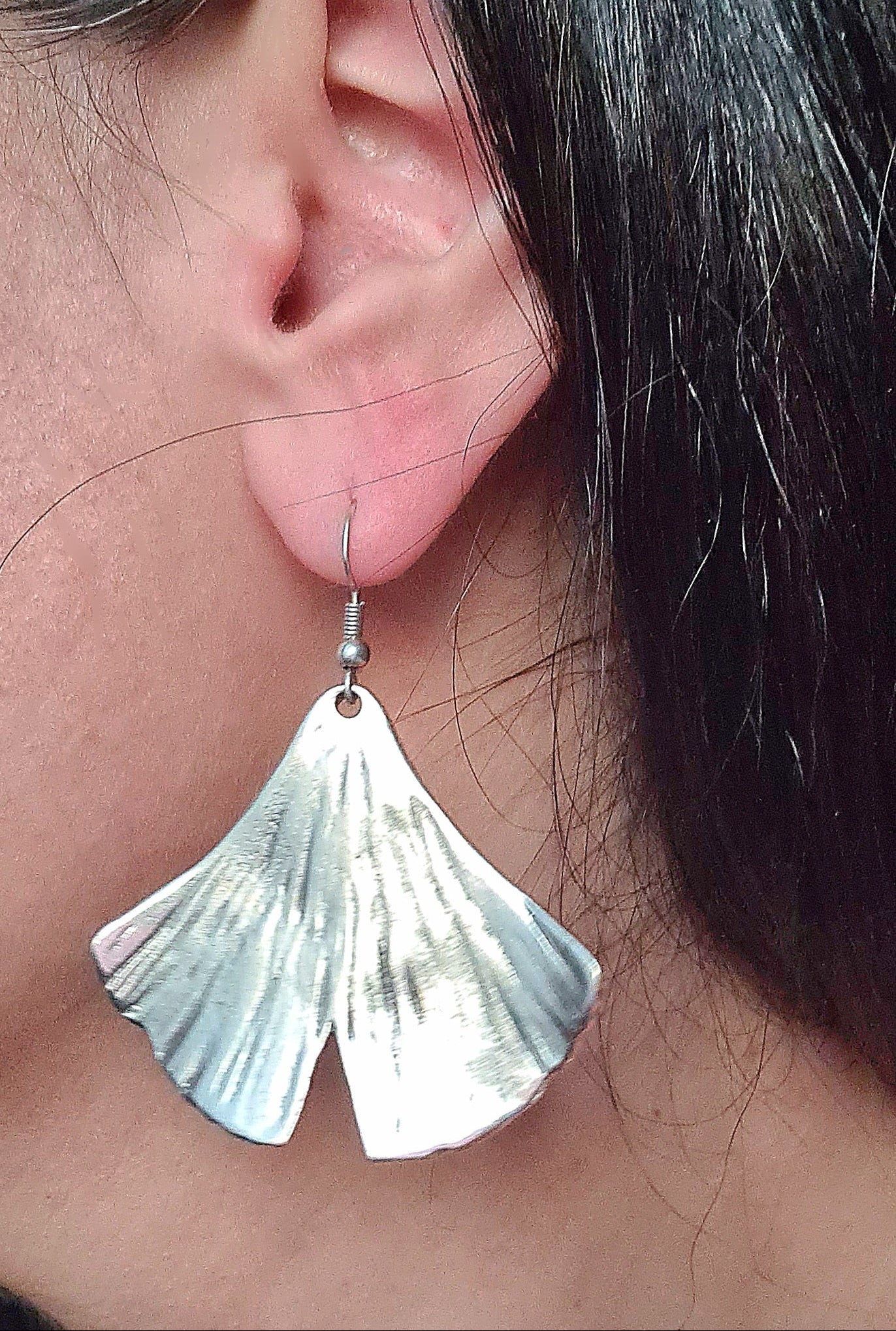 Extreme close-up macro shot of a silver ginkgo leaf earring on a model’s ear, highlighting the intricate metallic texture and premium craftsmanship.