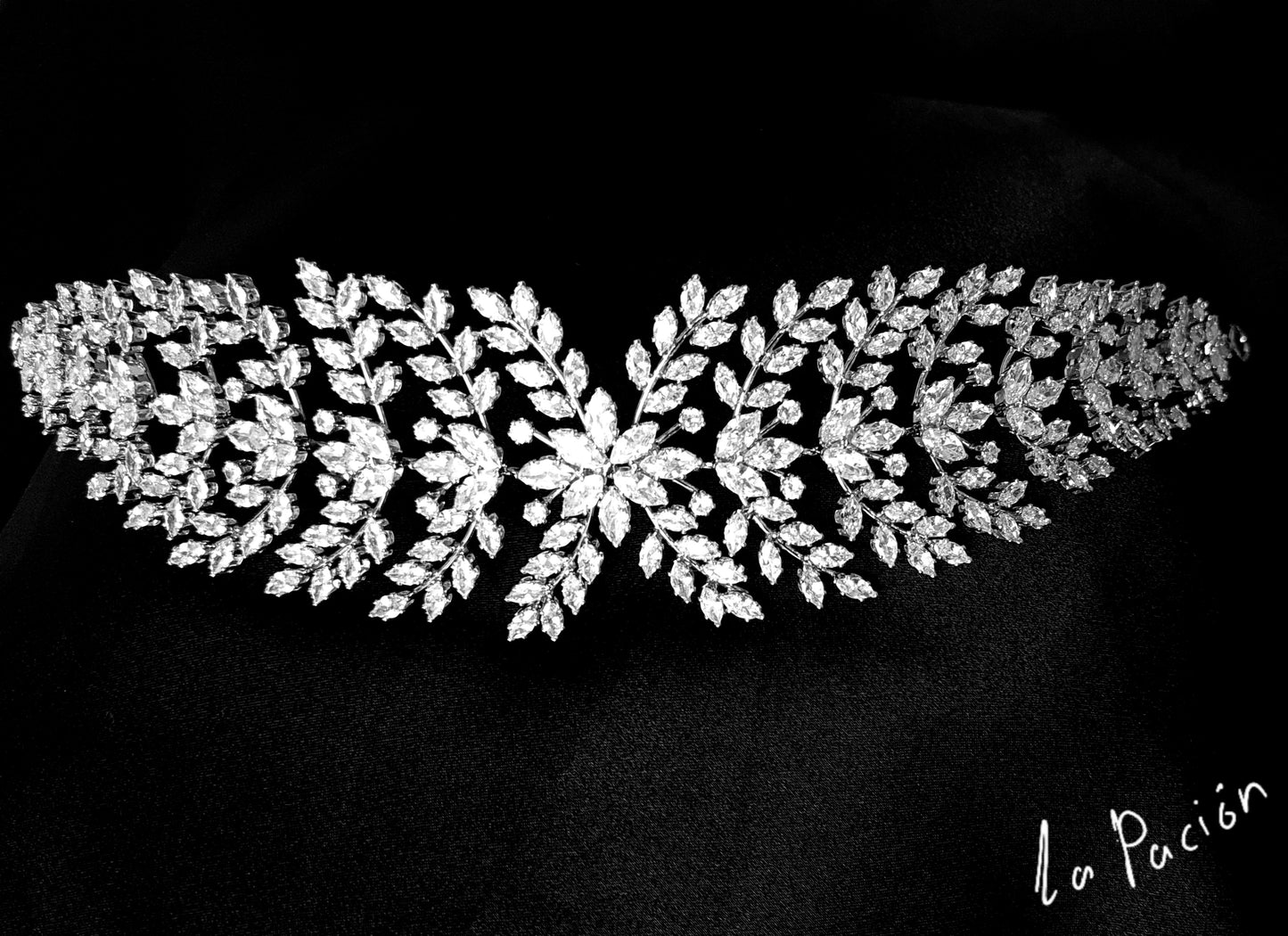 A wedding hair accessory made of metal and diamonds. The tiara has a delicate design with leaves and flowers. The diamonds are clear and sparkling. The background is black.