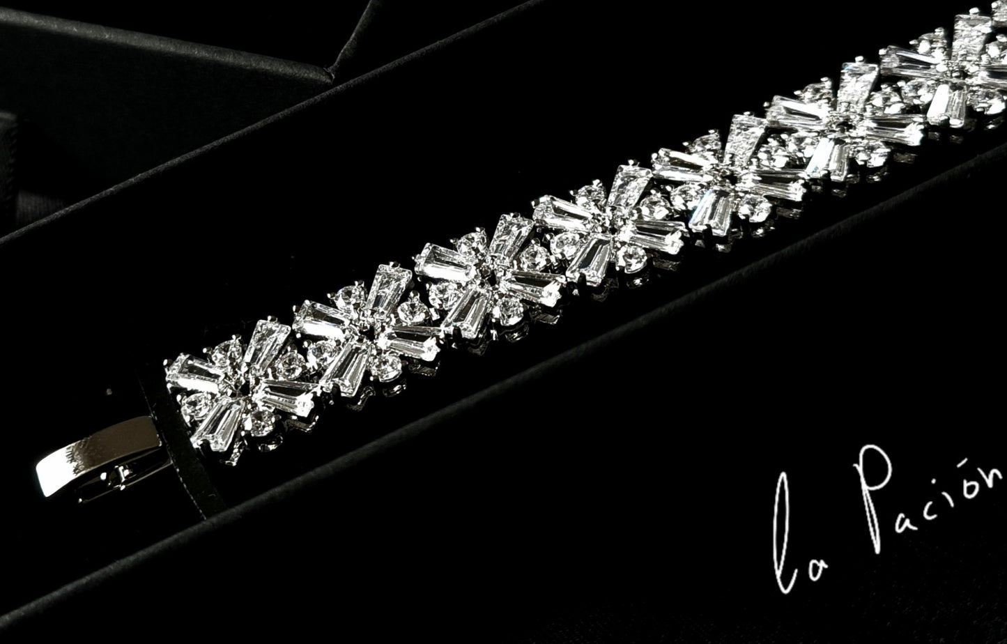 A bracelet with diamonds in a box on a black background. The bracelet is made of silver and has diamonds encrusted on it. The diamonds are sparkling and the bracelet is very shiny. The box is black.