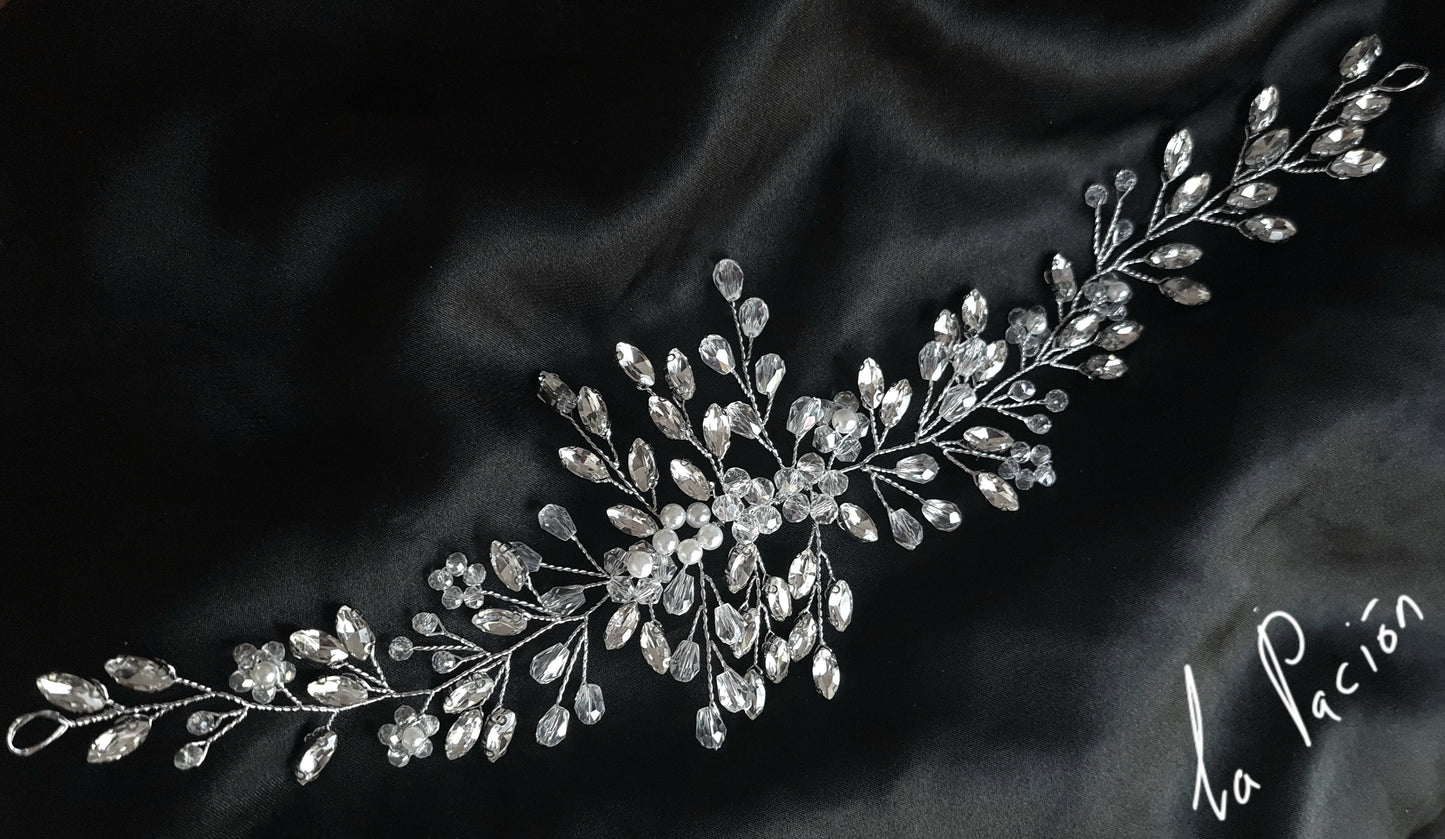 a bridal hair piece with pearls and crystals on a black background. The hair piece is made of pearls and crystals, and it has a delicate, feminine design. It is perfect for a bride who wants to add a touch of elegance to her wedding day look