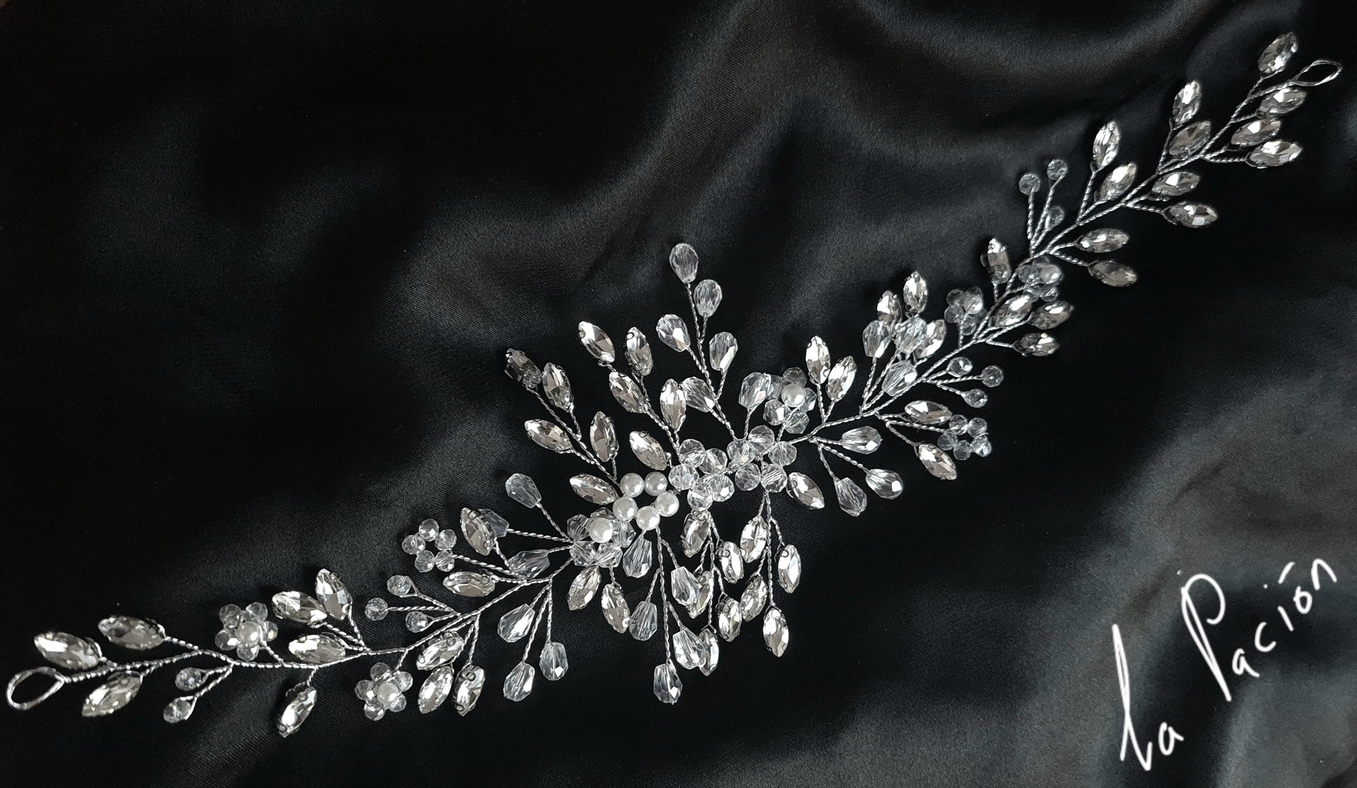 a bridal hair piece with pearls and crystals on a black background. The hair piece is made of pearls and crystals, and it has a delicate, feminine design. It is perfect for a bride who wants to add a touch of elegance to her wedding day look