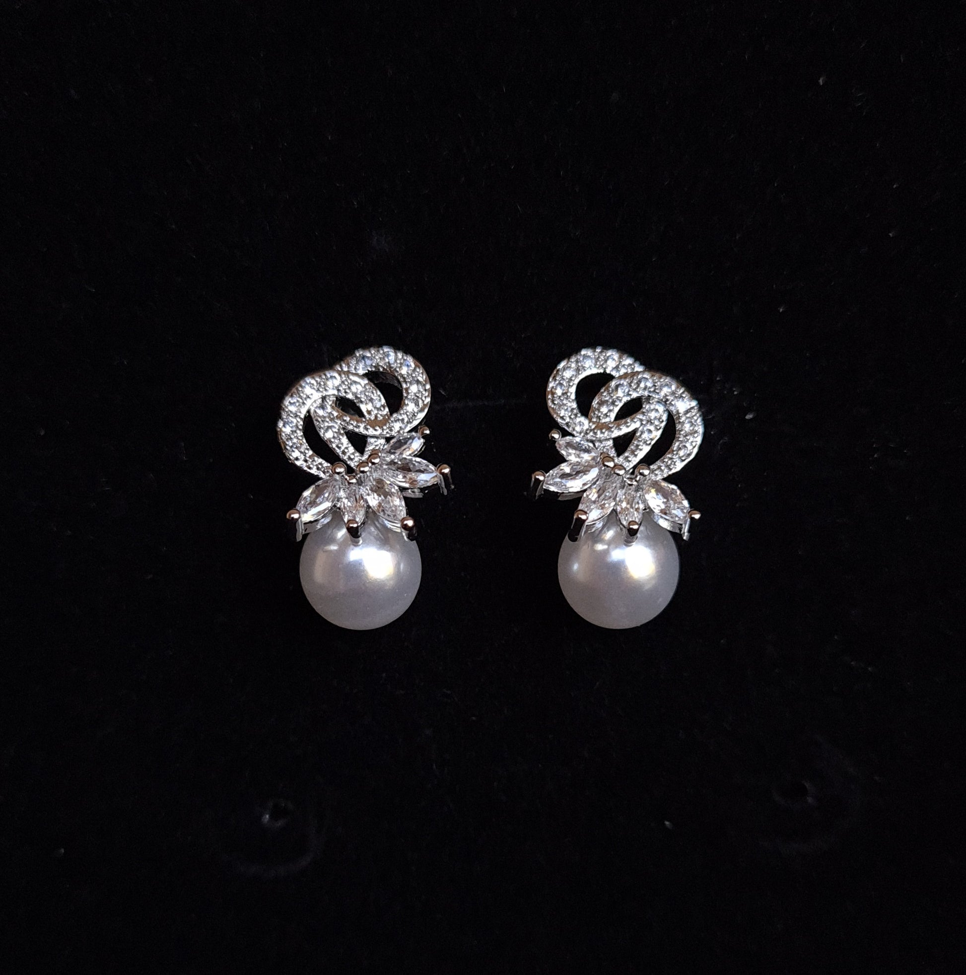 A pair of earrings with a pearl and rhinestones on a black background. The earrings are teardrop-shaped and have a simple, elegant design. The pearl is white and the rhinestones are clear.