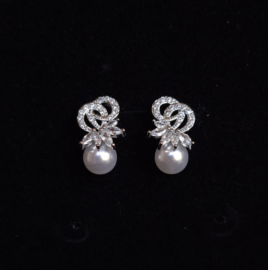 A pair of earrings with a pearl and rhinestones on a black background. The earrings are teardrop-shaped and have a simple, elegant design. The pearl is white and the rhinestones are clear.