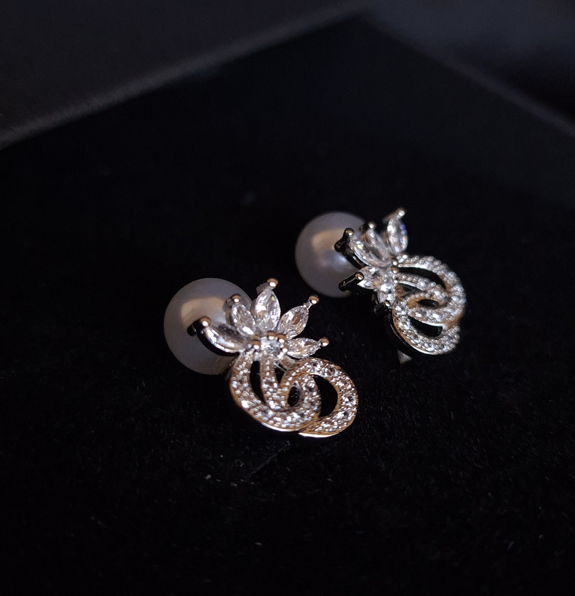 A pair of earrings with a pearl and rhinestones on a black background. The earrings are teardrop-shaped and have a simple, elegant design. The pearl is white and the rhinestones are clear.
