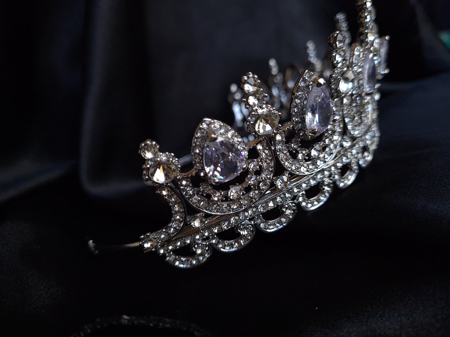 A close-up of a tiara made of cubic zirconia. The tiara is silver in color and has a cascading design. It is decorated with clear cubic zirconia stones that sparkle in the light.