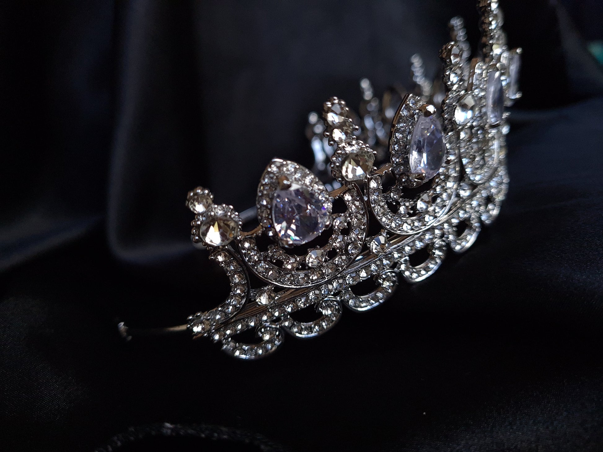 A close-up of a tiara made of cubic zirconia. The tiara is silver in color and has a cascading design. It is decorated with clear cubic zirconia stones that sparkle in the light.