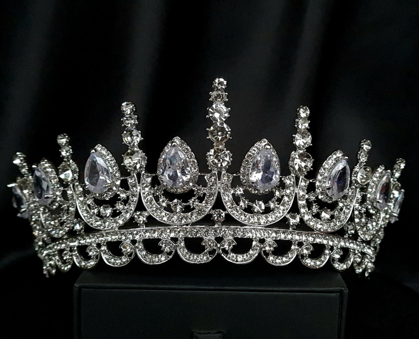 A close-up of a tiara made of cubic zirconia. The tiara is silver in color and has a cascading design. It is decorated with clear cubic zirconia stones that sparkle in the light.
