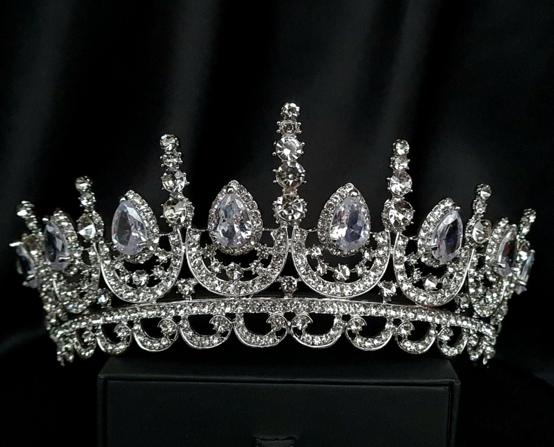 A close-up of a tiara made of cubic zirconia. The tiara is silver in color and has a cascading design. It is decorated with clear cubic zirconia stones that sparkle in the light.