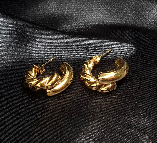 Gold hoop earrings sitting on black cloth. The earrings are a classic and elegant style that would be perfect for any occasion. The earrings are made of gold and have a hoop design. The hoops are large and round, and they sit on a black cloth.