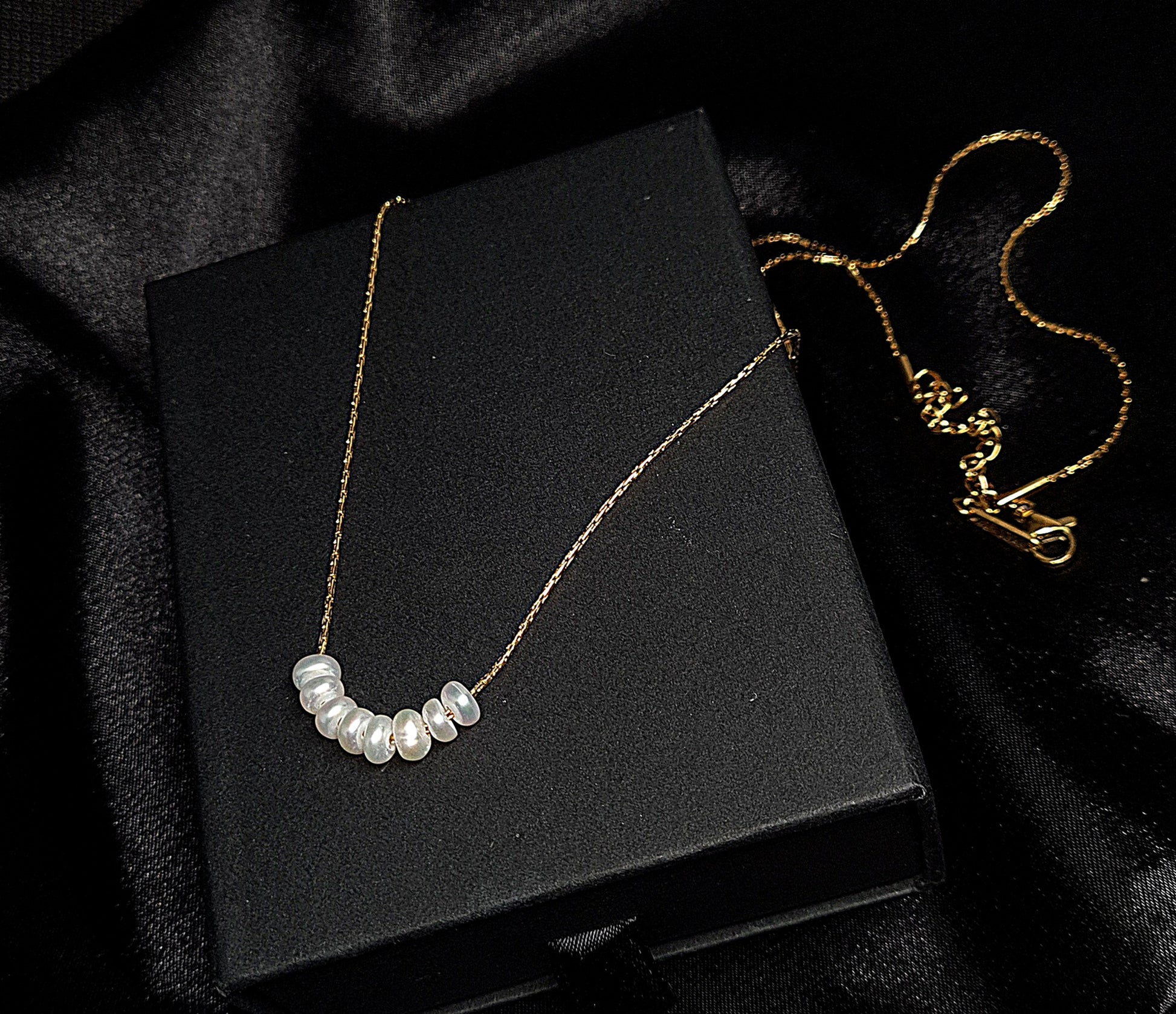 Pearl necklace sitting on black box. The necklace is made of pearls and has a simple design. The pearls are round and white, and they are strung on a black thread. The necklace is sitting on a black box, which provides a nice contrast to the white color of the pearls.