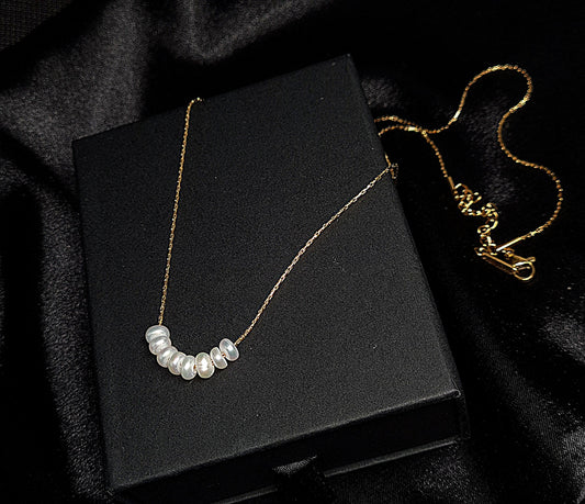 Pearl necklace sitting on black box. The necklace is made of pearls and has a simple design. The pearls are round and white, and they are strung on a black thread. The necklace is sitting on a black box, which provides a nice contrast to the white color of the pearls.