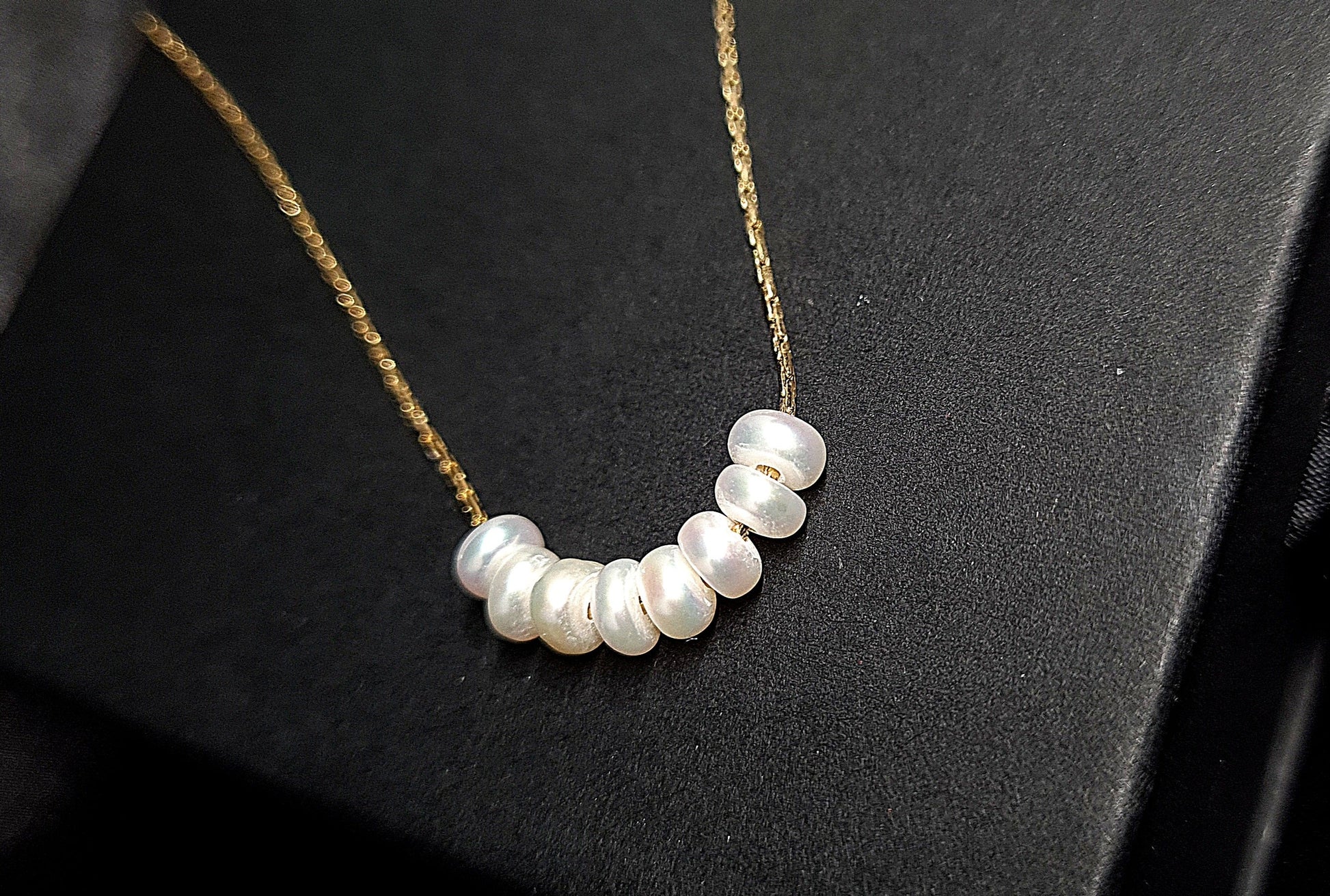Pearl necklace sitting on black box. The necklace is made of pearls and has a simple design. The pearls are round and white, and they are strung on a black thread. The necklace is sitting on a black box, which provides a nice contrast to the white color of the pearls.