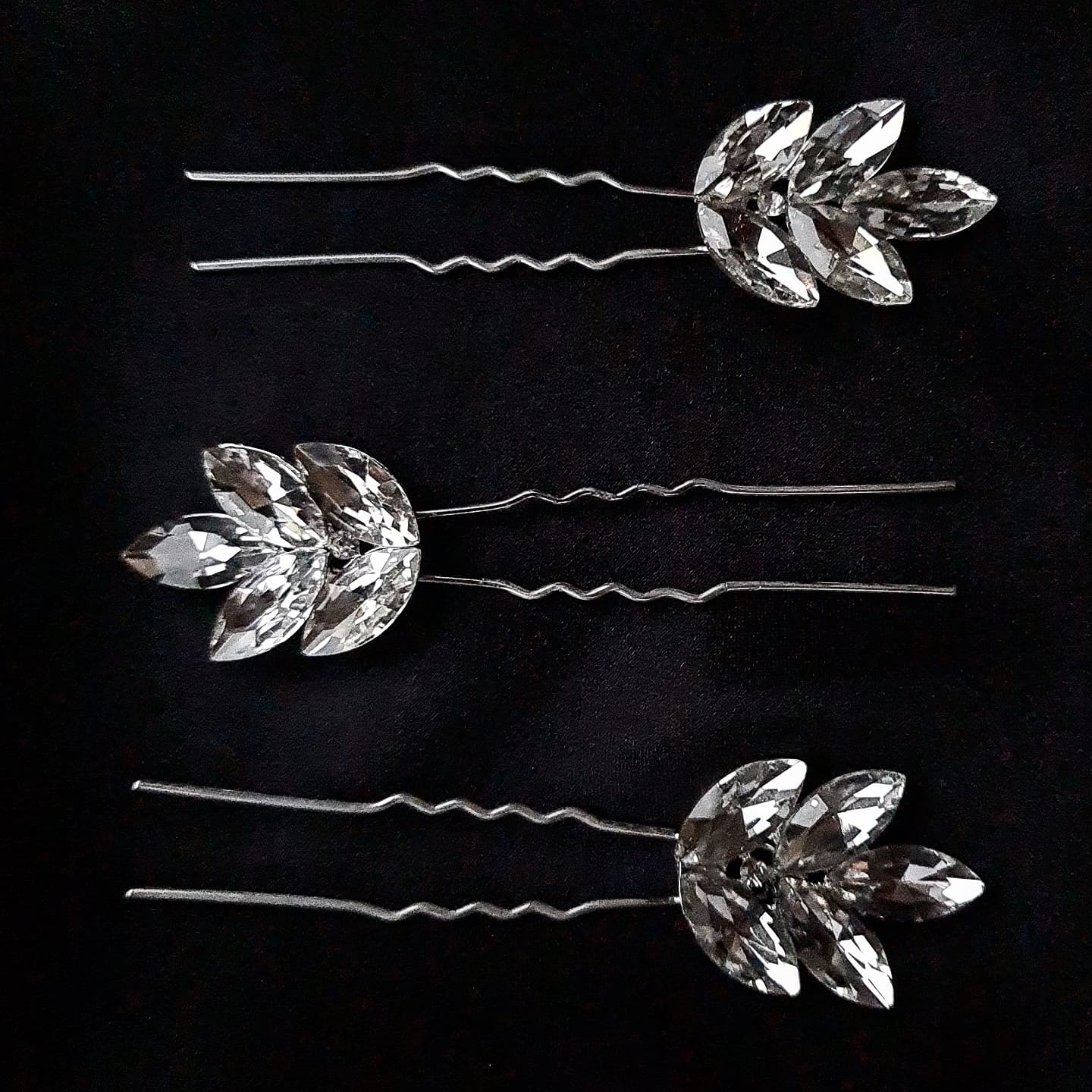 three hair pins with rhinestones on a black background. The hair pins are silver and have rhinestones of different sizes on them. The hair pins are in a triangular shape.