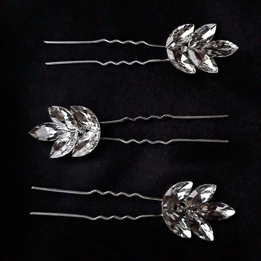 three hair pins with rhinestones on a black background. The hair pins are silver and have rhinestones of different sizes on them. The hair pins are in a triangular shape.