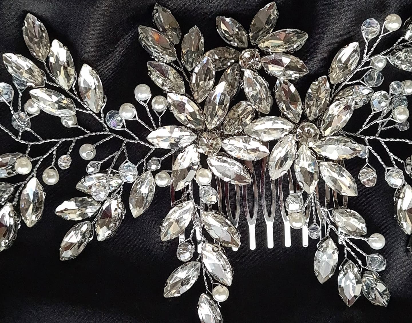 a close up view of A hair comb with rhinestones and leaves on a black background. It has a delicate design with leaves and flowers. The rhinestones are clear and sparkling. The background is black.