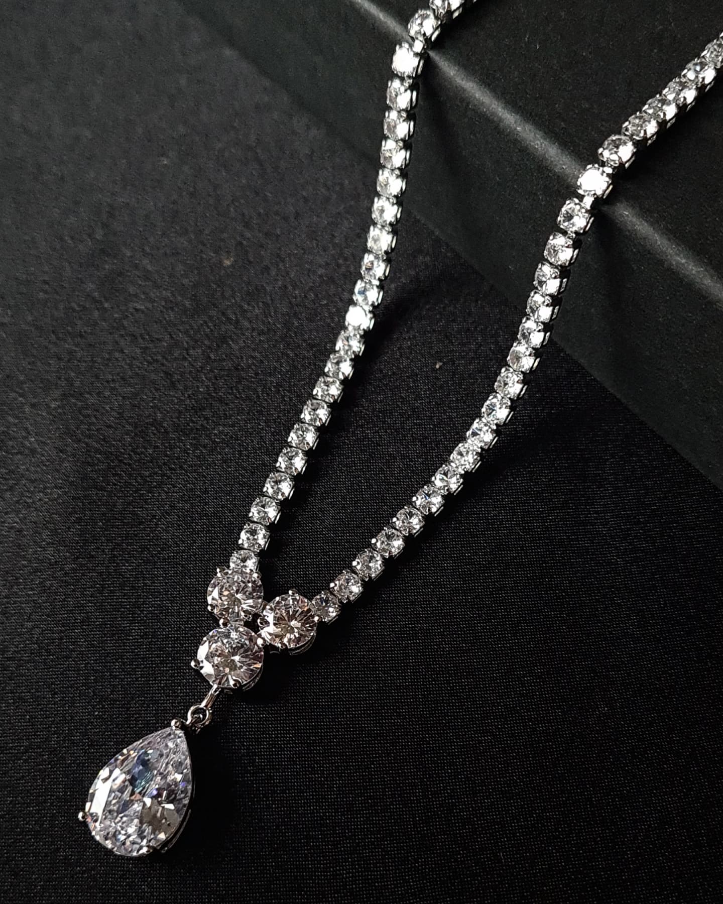 Close-up view of a diamond necklace sparkling with zirconia Diamonds displayed on a black table. the center piece is tear drop shape zirconia stone.
