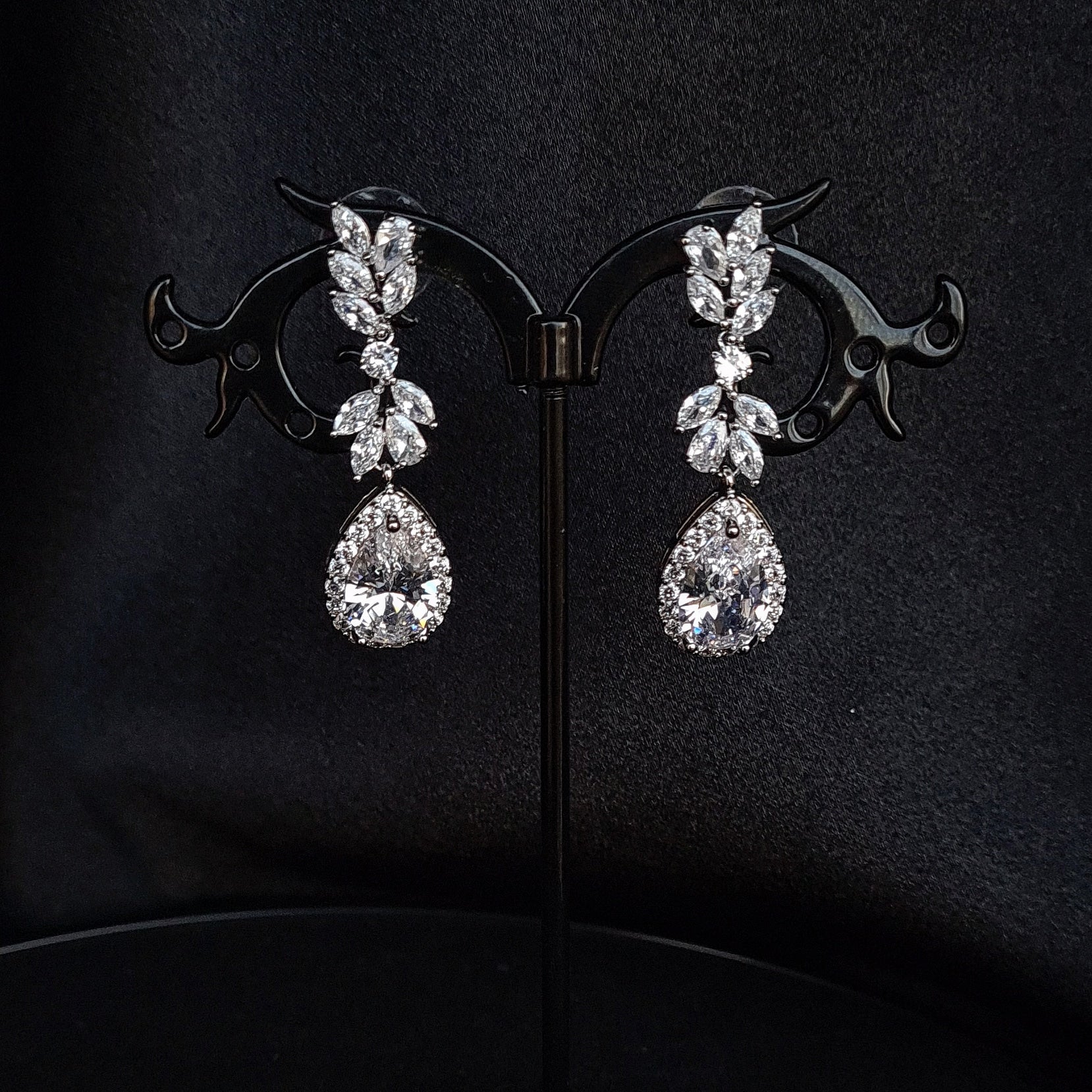 A pair of silver earrings with dangling teardrop pearls. The earrings are simple in design and the pearls are lustrous. The earrings are a perfect accessory for a special occasion or a gift for a loved one.