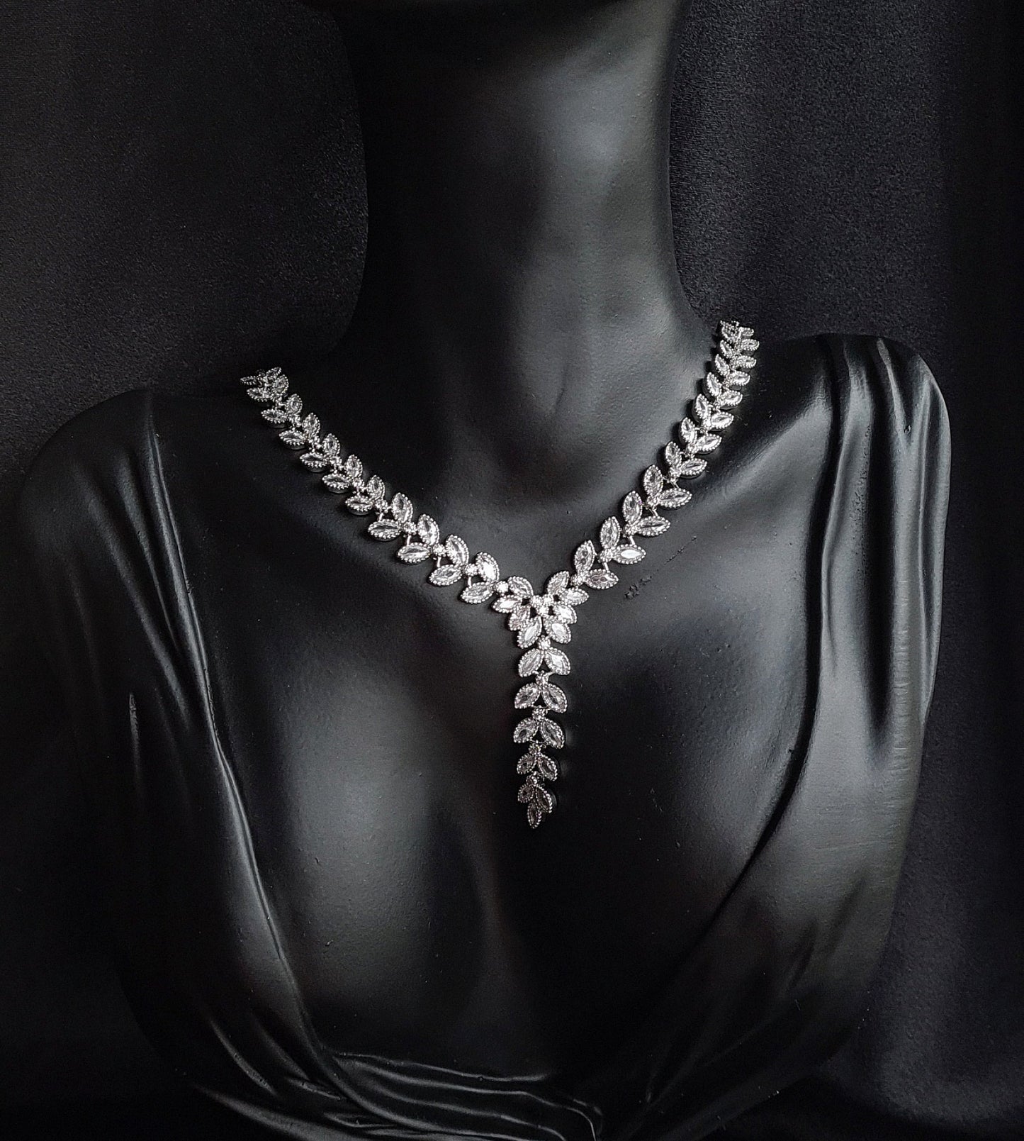 a necklace with cubic zirconia stones. The necklace is made of white silver and has cubic zirconia stones in a variety of shapes and sizes. The necklace is the main focus of the image and it sparkles in the light