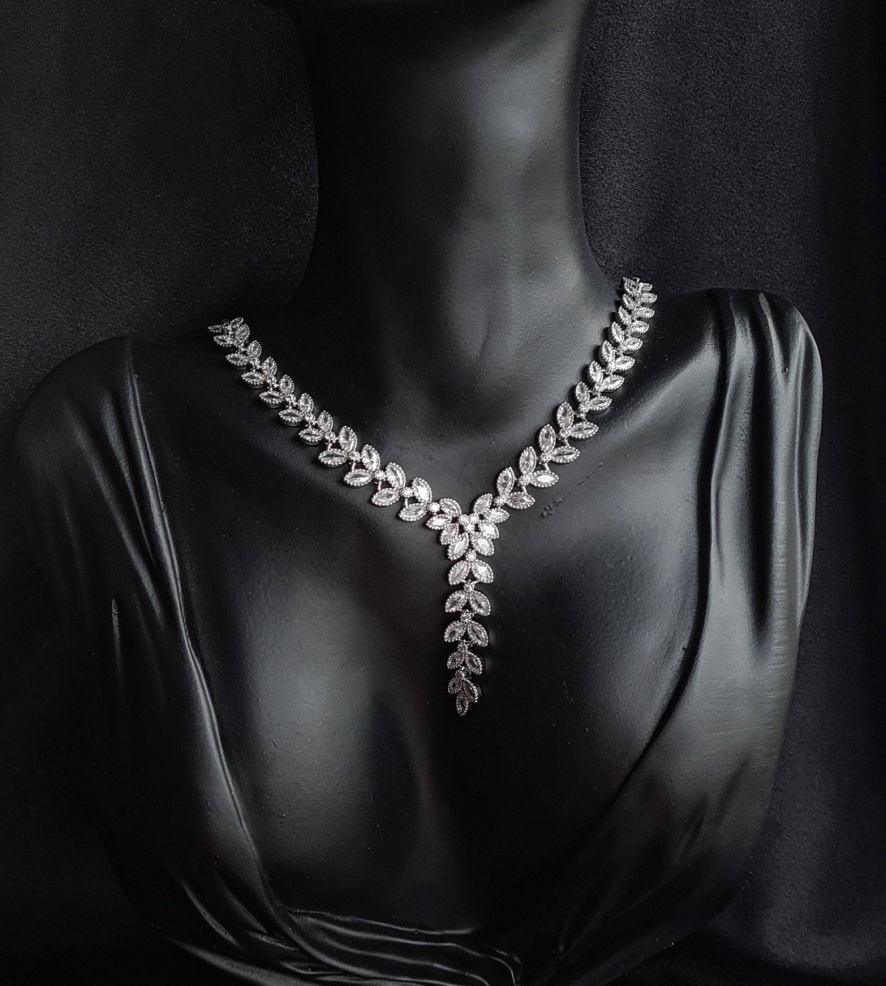 a necklace with cubic zirconia stones. The necklace is made of white silver and has cubic zirconia stones in a variety of shapes and sizes. The necklace is the main focus of the image and it sparkles in the light