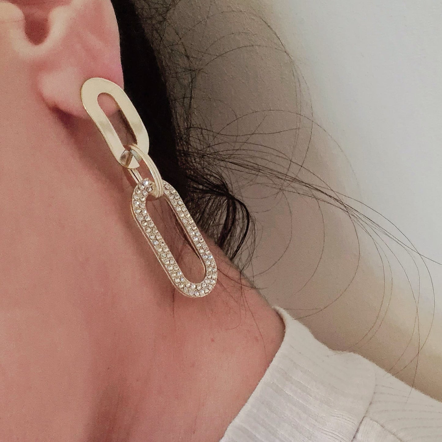 a woman wearing A pair of gold earrings with rhinestones. The earrings are teardrop-shaped with a gold border. The rhinestones are clear and round. The background is a white.