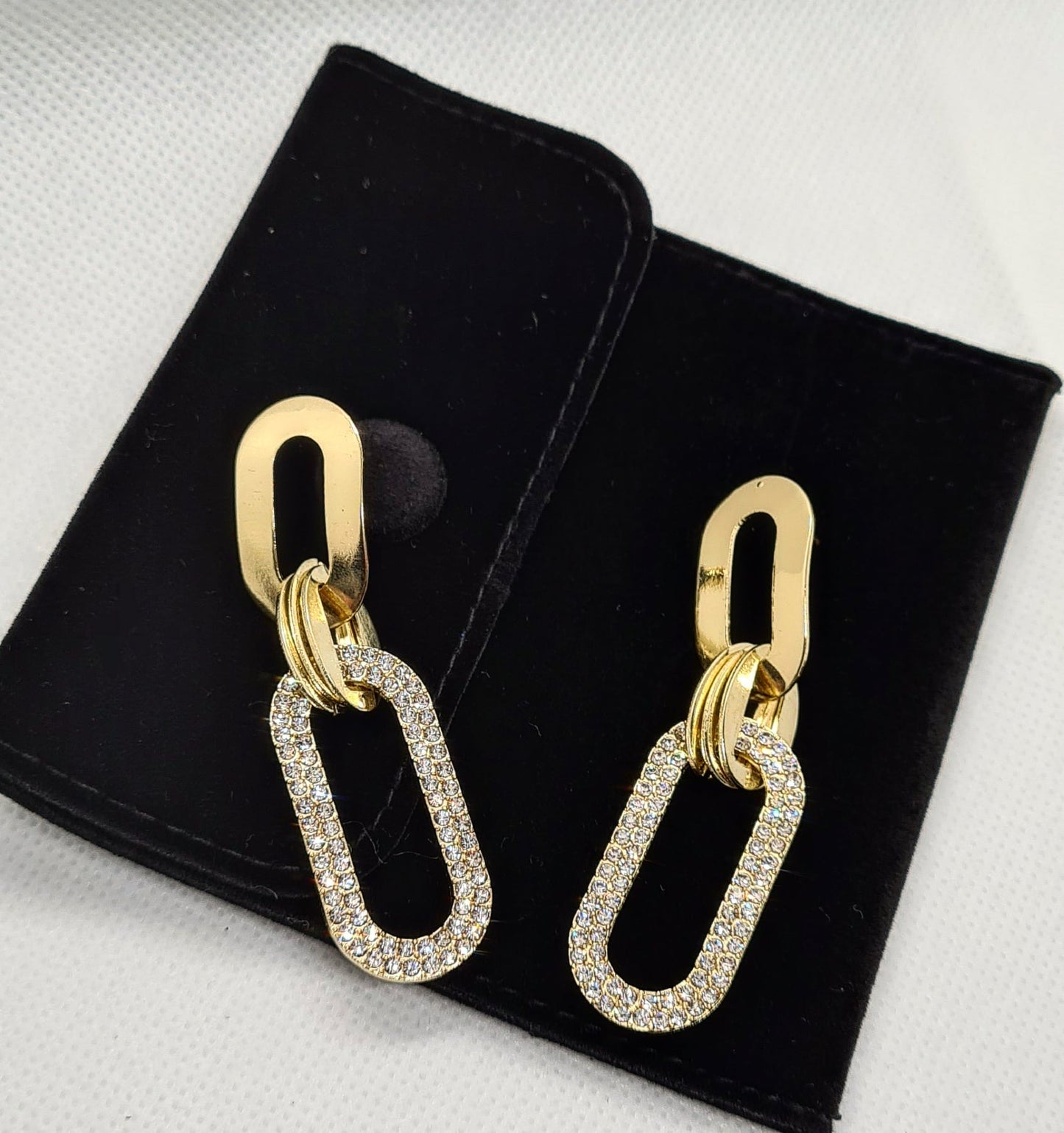 A pair of gold earrings with rhinestones on a white background. The earrings are teardrop-shaped with a gold border. The rhinestones are clear and round. The background is a white.