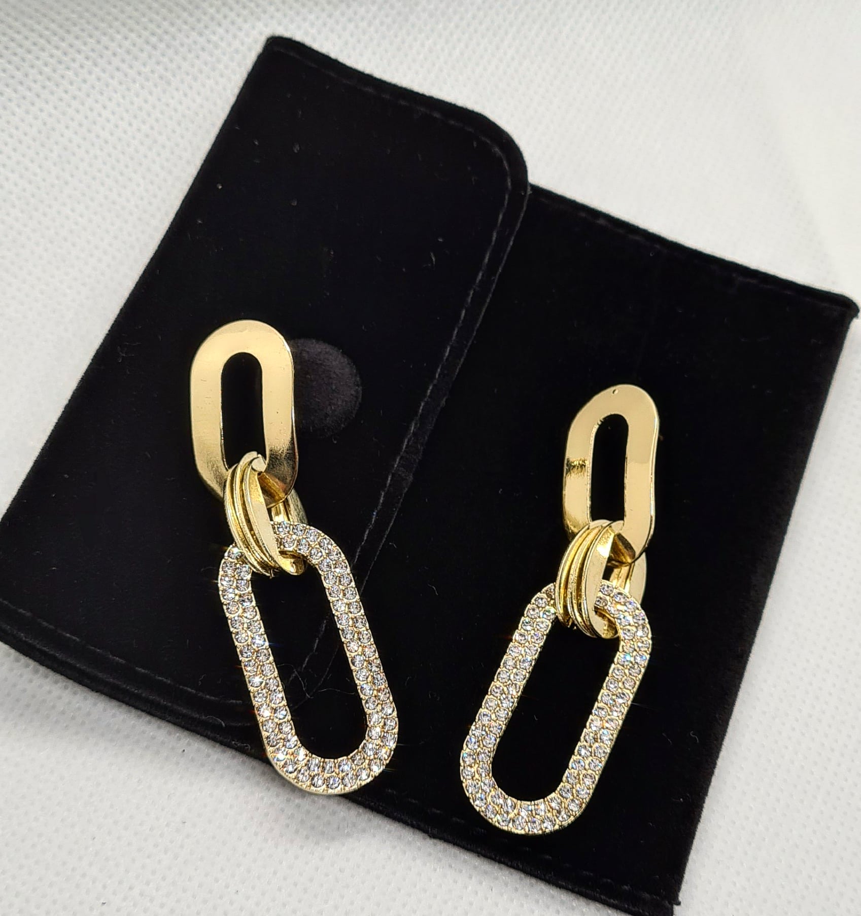 A pair of gold earrings with rhinestones on a white background. The earrings are teardrop-shaped with a gold border. The rhinestones are clear and round. The background is a white.