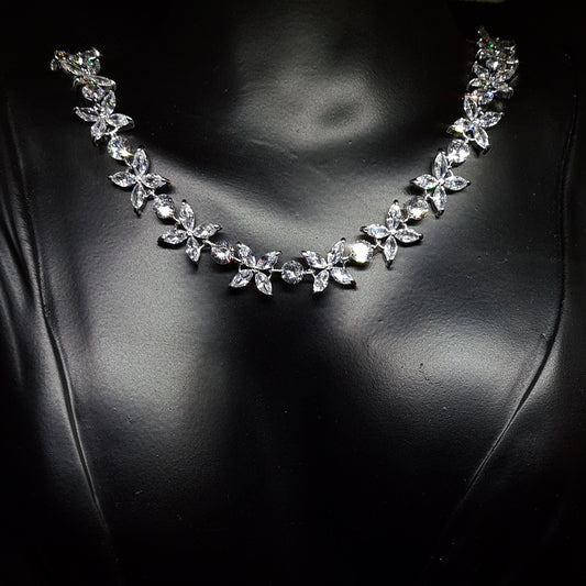 Close-up of a necklace on a mannequin. The necklace is made up of multiple strands of cubic zirconia, with a large pendant in the center. The pendant is flower-shaped and has a sparkling cubic zirconia in the center. The necklace is resting on the mannequin's neck,
