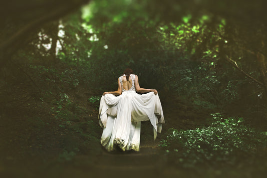 A woman lifting up the ends of her white wedding dress on a forest path.