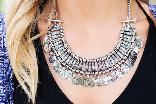 a close-up shot of a women with blonde hair wearing a filigree silver necklace with black blouse.