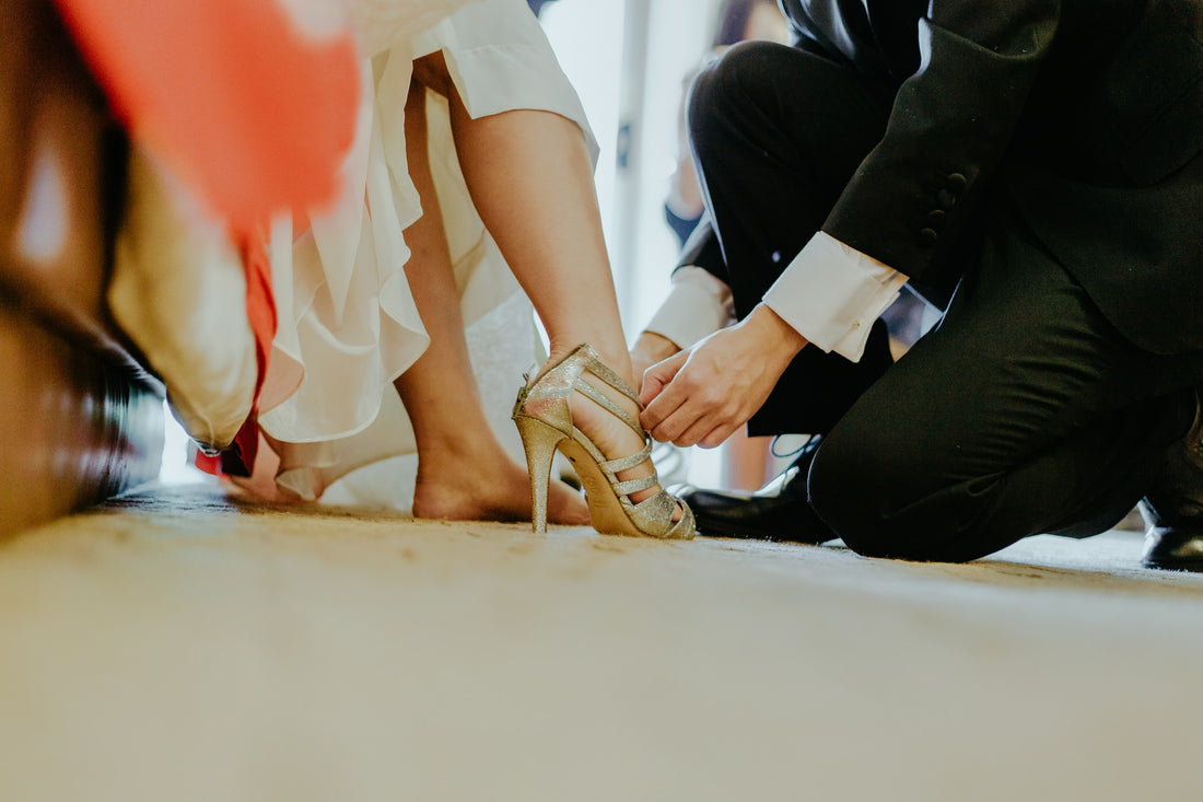a close shot of a groom helping a bride putting on heels 