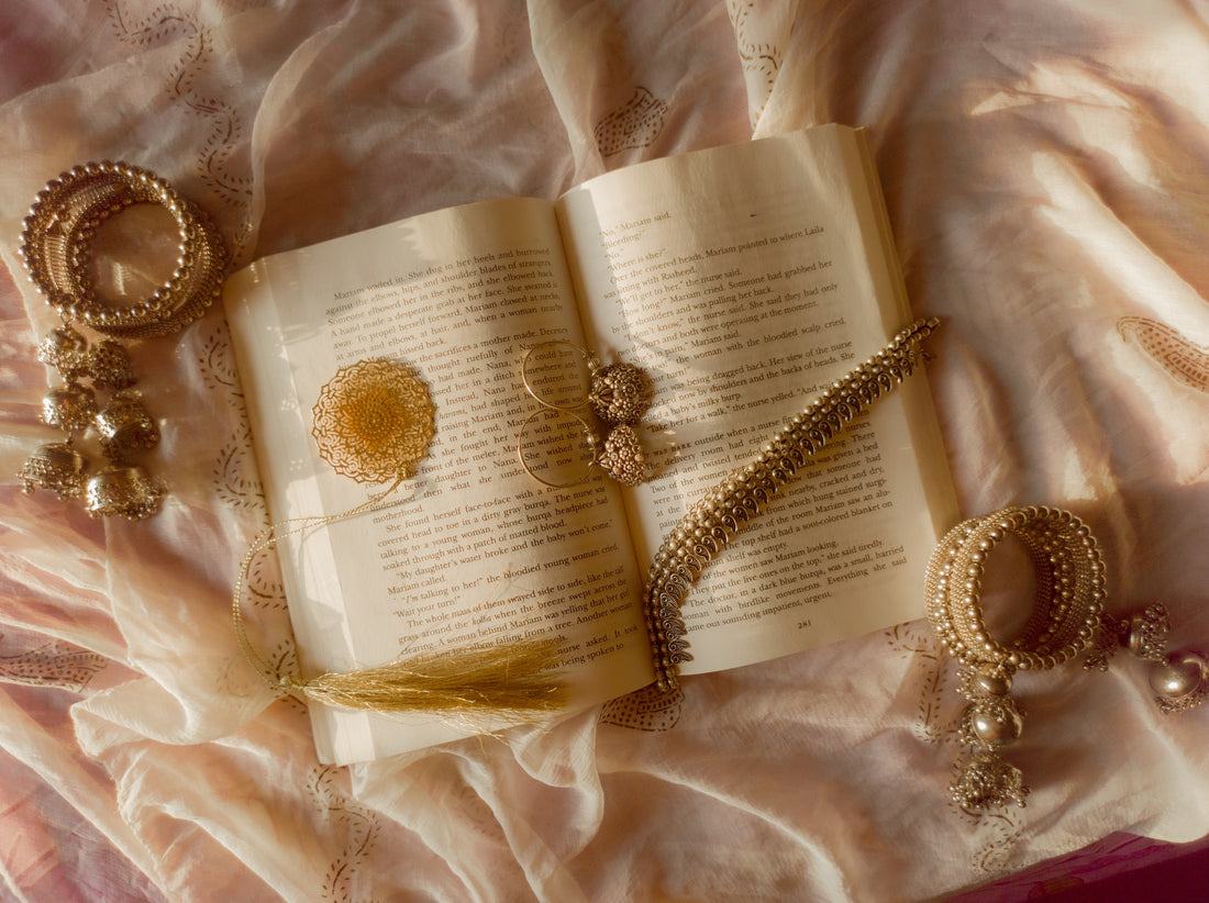 a book lying on a bed surrounded by jewelry items.