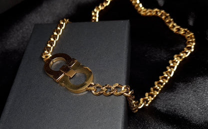 A gold chain necklace with the letter C on it sitting on top of a black box. The necklace is made of gold and has a simple design. The letter C is large and has a polished finish. The necklace is elegant and understated.
