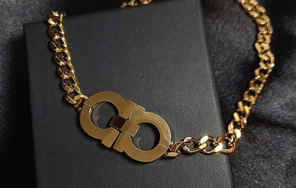 A gold chain necklace with the letter C on it sitting on top of a black box. The necklace is made of gold and has a simple design. The letter C is large and has a polished finish. The necklace is elegant and understated.