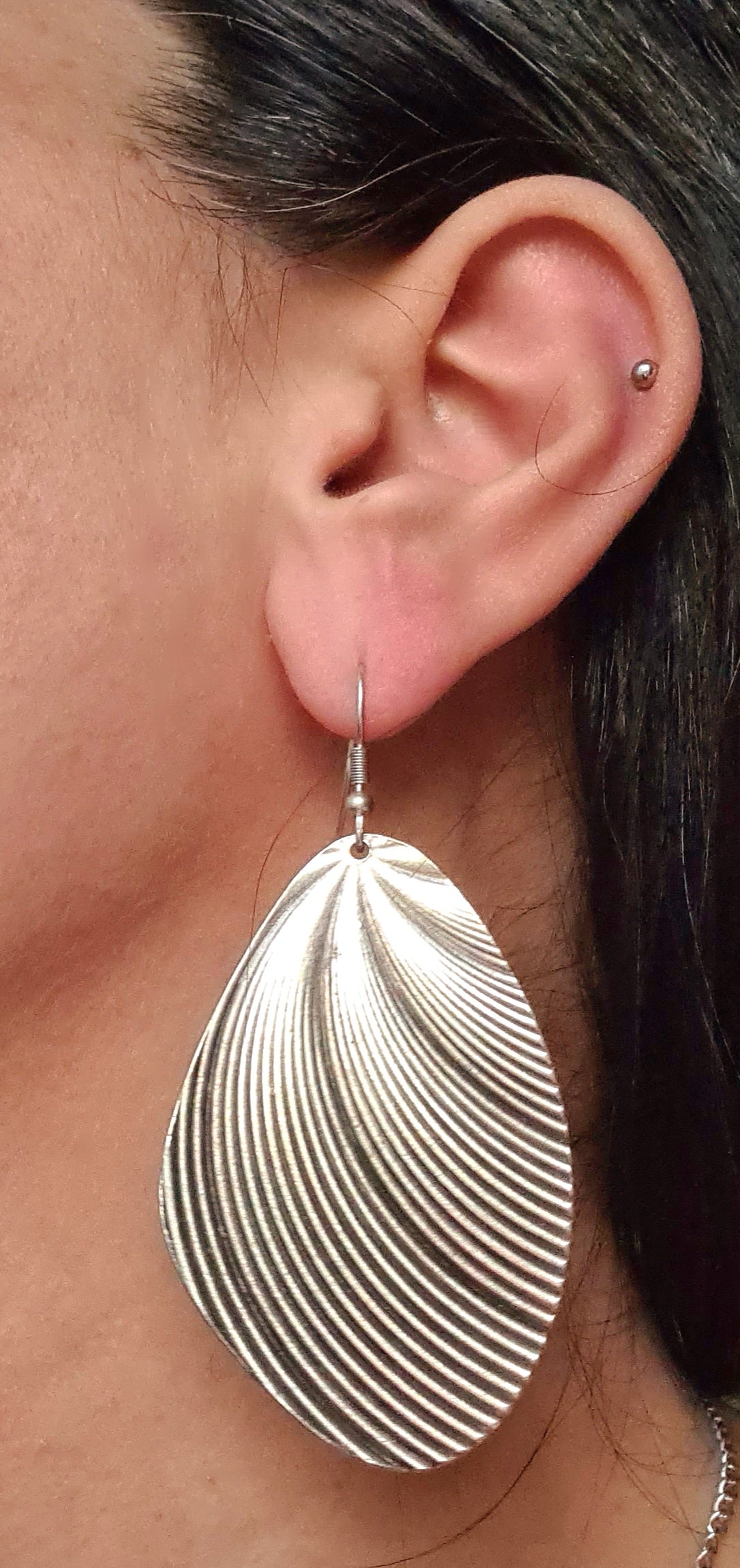 A woman wearing silver earrings. The earrings are small and delicate, and they have a oval design on them. The earrings are on the woman's ears, and they are reflecting the light.