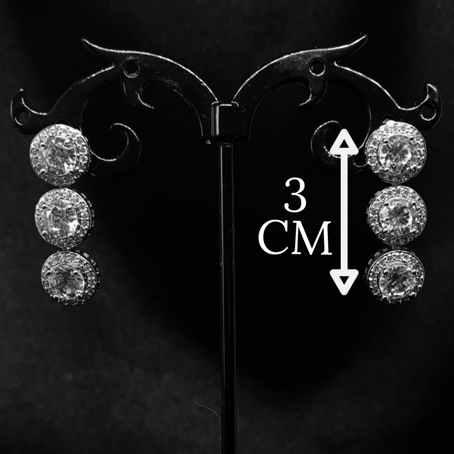 A pair of dangle earrings made of cubic zirconia. The earrings are round-shaped and have a simple, elegant design. The cubic zirconia stones are clear and sparkling. The earrings are hanging from a black metal wire. with measure.