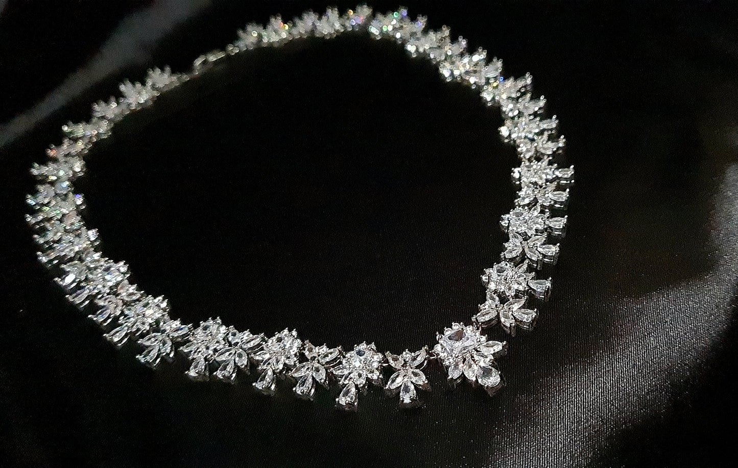 Image of a diamond necklace on a black cloth. The necklace is made up of multiple strands of diamonds, with a large pendant in the center. The diamonds are sparkling in the light, and the black cloth provides a striking contrast.